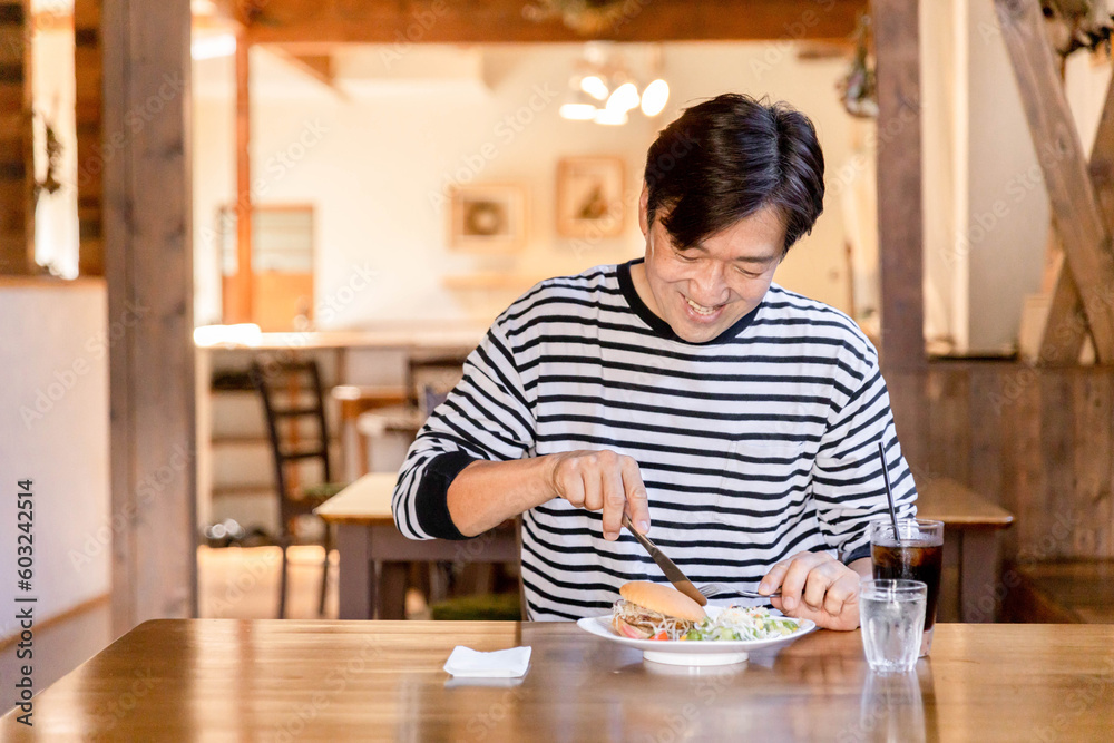 Fototapeta premium ランチ・昼食にカフェでハンバーガーをフォークとナイフで食べる男性
