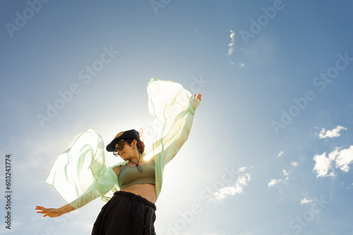 woman with scarf, handkerchief, cap and sunglasses at sunset, lens flare, wind clouds background smiling face blue sky dancing