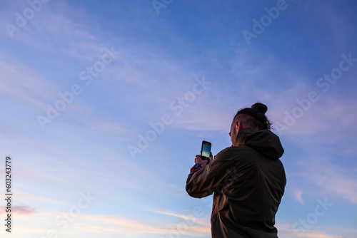 long-haired man taking mobile phone pictures of the sunset with purple, purple, orange, and blue colors