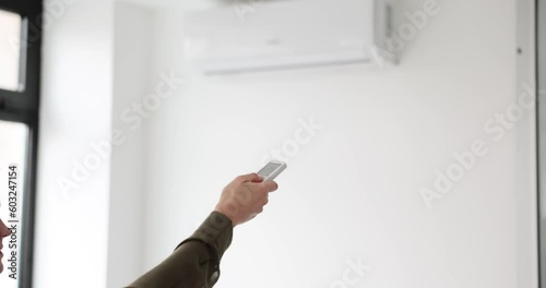 Female person stabilises temperature in office with remote control. Woman uses air conditioner to cool or heat air for comfortable work at home slow motion photo