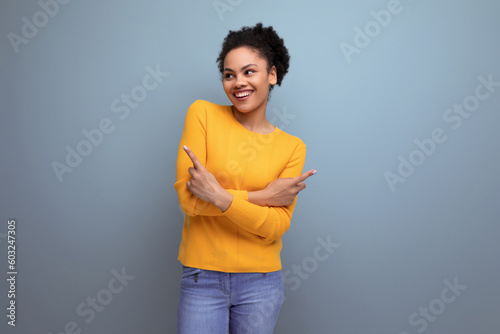 smart young latin woman with afro hair pointing finger to the side on gray background with copy space