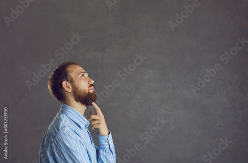 Serious young man thinking of solution to problem standing isolated on grey copyspace background. Business executive doubting and hesitating unsure of what decision to take. Side view profile portrait