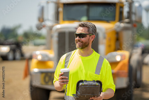 Men driver near lorry truck. Man truck driver in safety vest near truck. Happy hispanic man trucker trucking owner. Man driver with lunch box. Truck driver having take away lunch drink coffee to go. photo