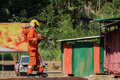 A firefighter is standing sideways and holding an iron ax in an outdoors location.