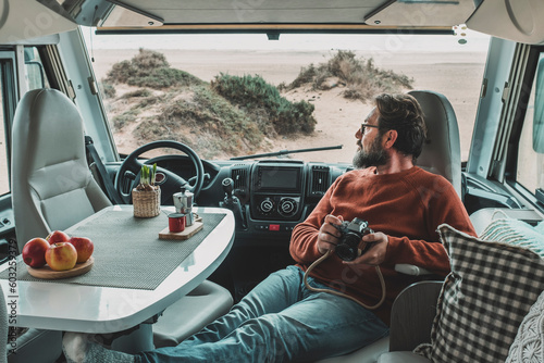 Travel lifestyle and vanlife. Tourist enjoy and relax on vacation sitting inside motorhome vehicle and using photo camera. Traveler photographer. People and adventure. Parking at the beach. Camper van