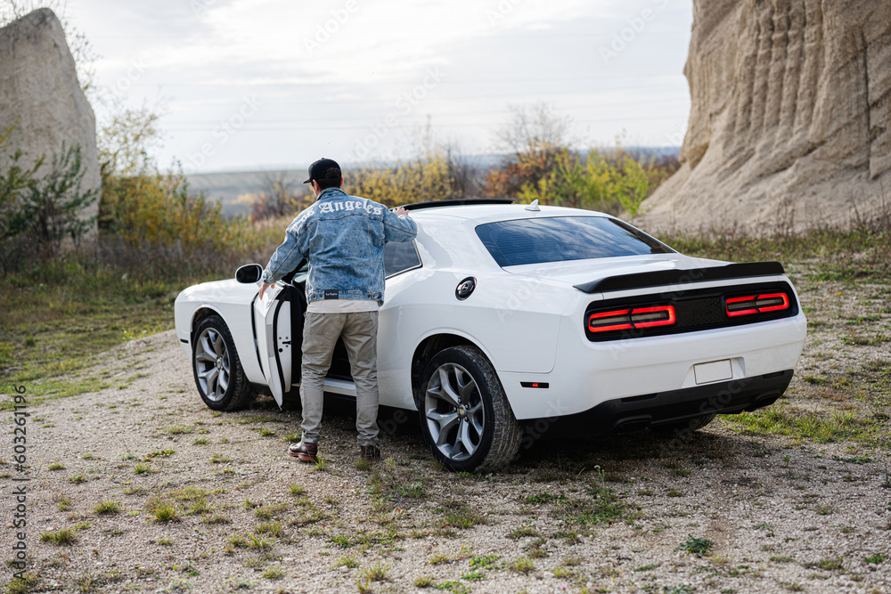 Handsome man in jeans jacket and cap sitting in his white muscle car in career. Handsome man in jeans jacket and cap sitting in his white muscle car in career.