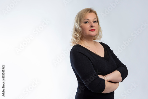 Alluring Winsome Mature Confident Caucasian Woman in Black Blazer With Hands Folded Over White Background.