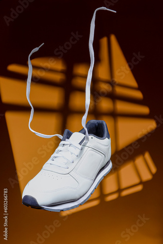 Pair of New White Sneaker With Flying Shoelaces Placed Over Yellow Background With Sportlight.