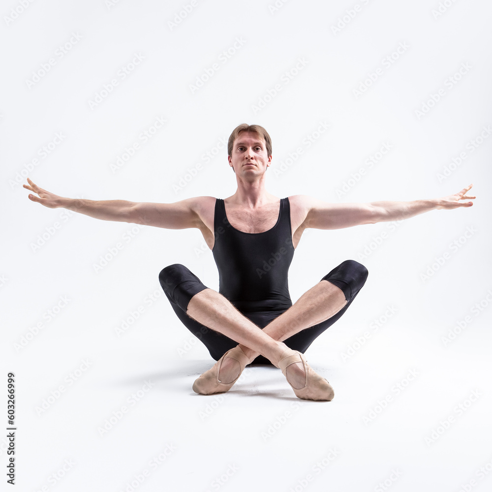 Male Ballerino Dancer Sitting While Practising Legs and Arms Stretching Exercices In Black Sportive Tights in Studio.