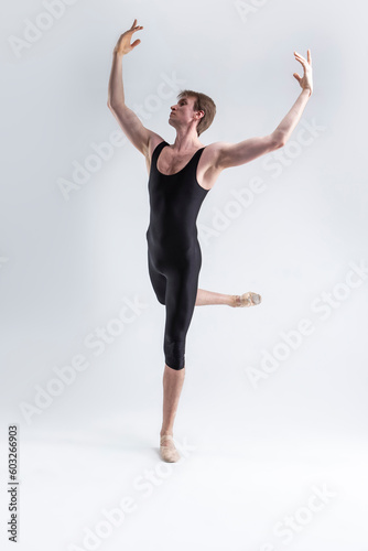 Sports Ideas. Young Athletic Caucasian Ballet Dancer Man Posing in Dancing Stretching Pose With Hands Lifted Up in Black Tights On White.