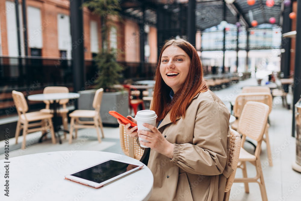 Young woman enjoying a coffee, sitting on the cafe terrace on the modern city street. Person sitting at table and using smartphone outdoors. Online education, order, working or shopping concept Young woman enjoying a coffee, sitting on the cafe terrace on the modern city street. Person sitting at table and using smartphone outdoors. Online education, order, working or shopping concept
