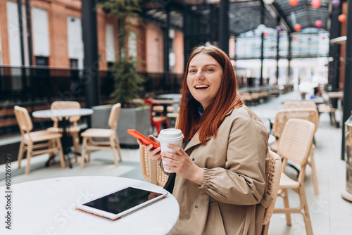 Young woman enjoying a coffee, sitting on the cafe terrace on the modern city street. Person sitting at table and using smartphone outdoors. Online education, order, working or shopping concept