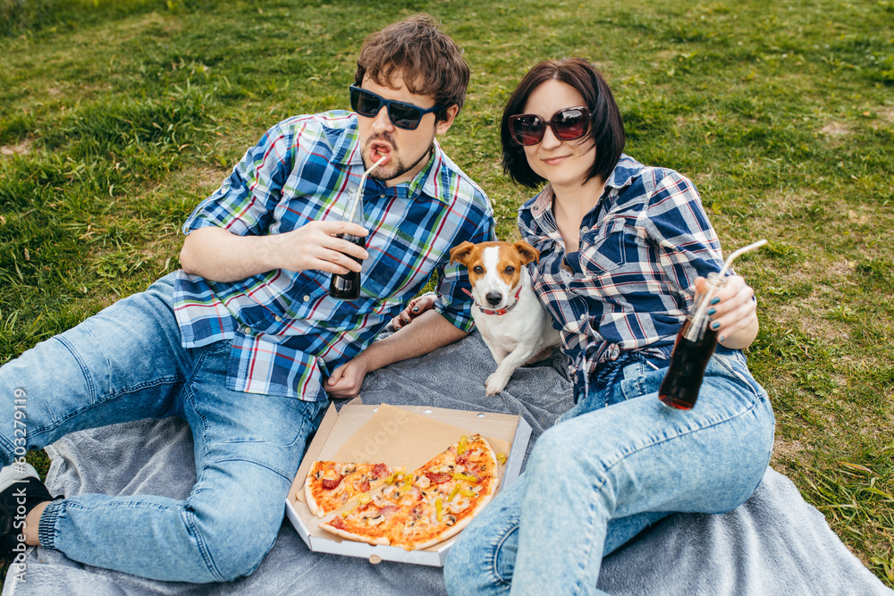 Obraz premium Adult stylish couple sitting at trunk of car and eating pizza snack outdoor