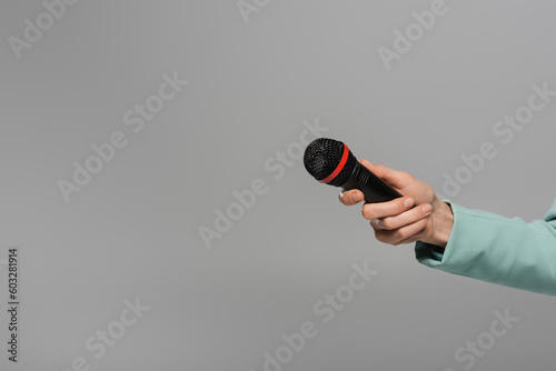 Cropped view of hand of host of event in blue jacket holding black and wireless microphone during holiday while standing isolated on grey