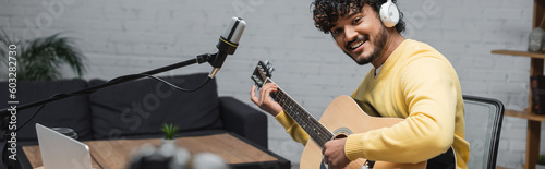 Canvas Print curly and happy indian musician in headphones and yellow jumper playing acoustic