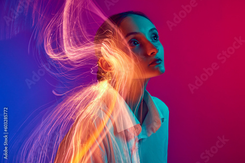 Portrait of young girl posing over gradient blue pink studio background with neon lights effect. Creative vision. Concept of art, modern style, cyberpunk, futurism and creativity