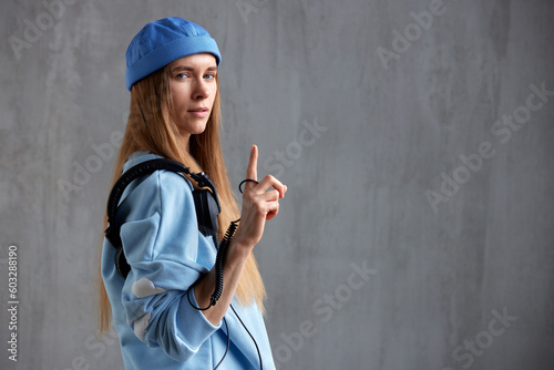 Half-length portrait of a young pretty long-haired girl in a blue sweater and cap with DJ headphones on her shoulder. Music, fun and beauty. Copy space.