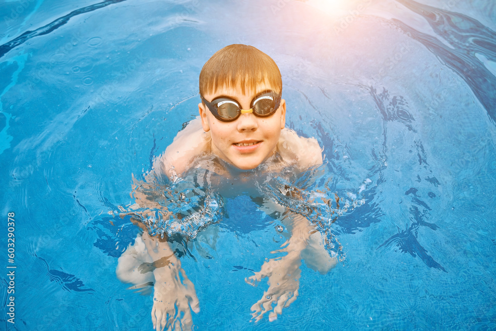Naklejka premium Smiling boy portrait in swimming goggles, Child swim in the pool, sunbathes, swimming in hot summer day. Relax, Travel, Holidays, Freedom concept.