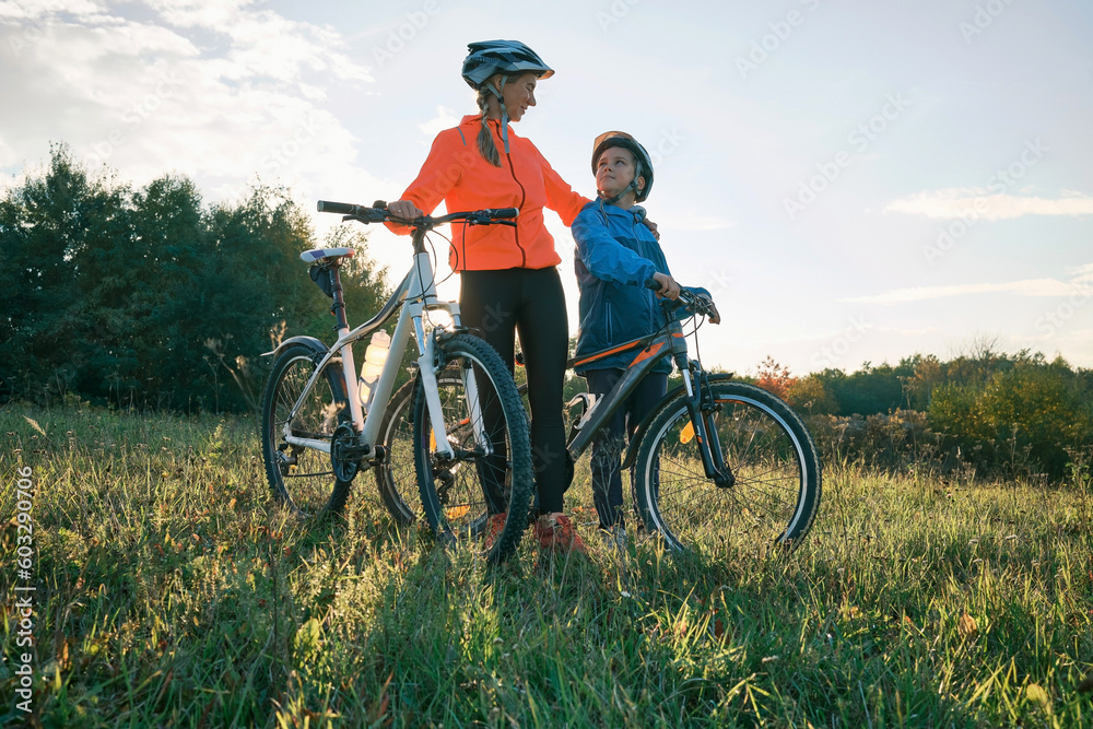 Mother and son ride bike outdoors. Happy cute boy in helmet to riding a bike in park on green meadow at sunset time. Family weekend. mothers Day
