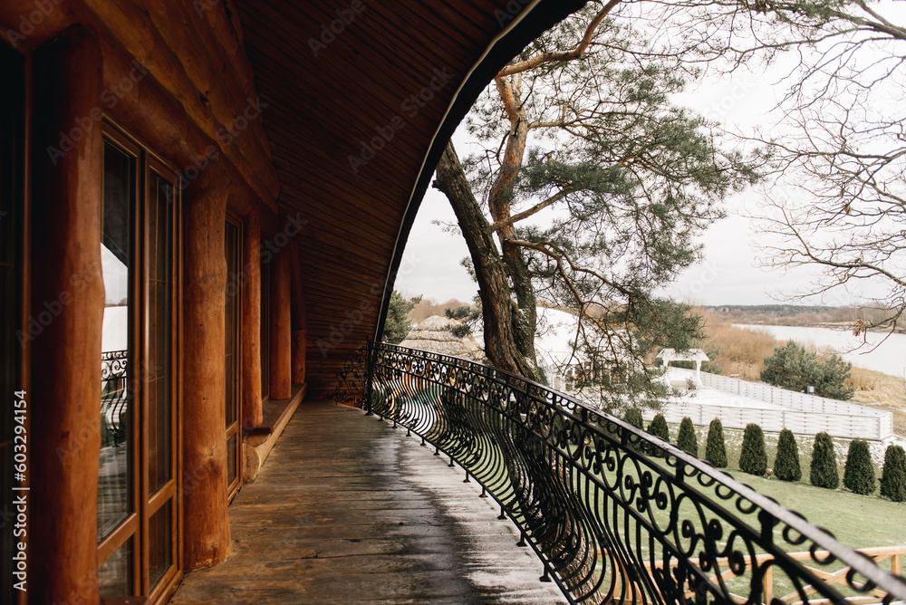 Obraz premium A large semicircular balcony of a wooden house with wrought iron railings and a beautiful view of nature and the river