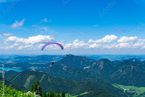 Paraglider flying over mountains and valleys on a summer, clear, day. Spectacular view of the Alps and Salzkammergut peak mountains and lake. Paragliding over a wild breathtaking nature.