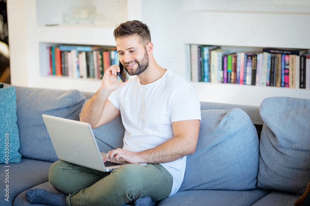 MId aged man wearing casual clothes and having a call and using laptop at home MId aged man wearing casual clothes and having a call and using laptop at home