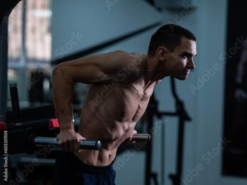 Shirtless man doing triceps dips from parallel bars in gym. 