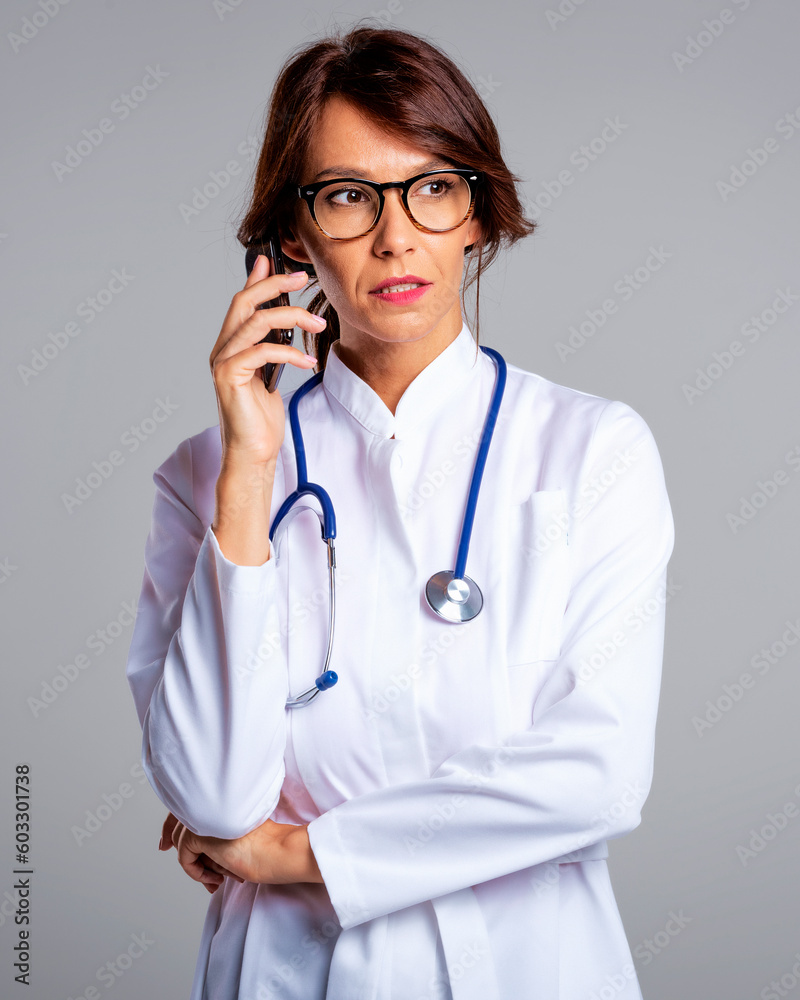 Studio portrait of middle aged female doctor using cellphone and standing at isolated background Studio portrait of middle aged female doctor using cellphone and standing at isolated background