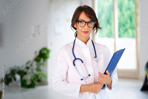 Smiling female doctor standing at the hospital and holding a clipboard in her hand
