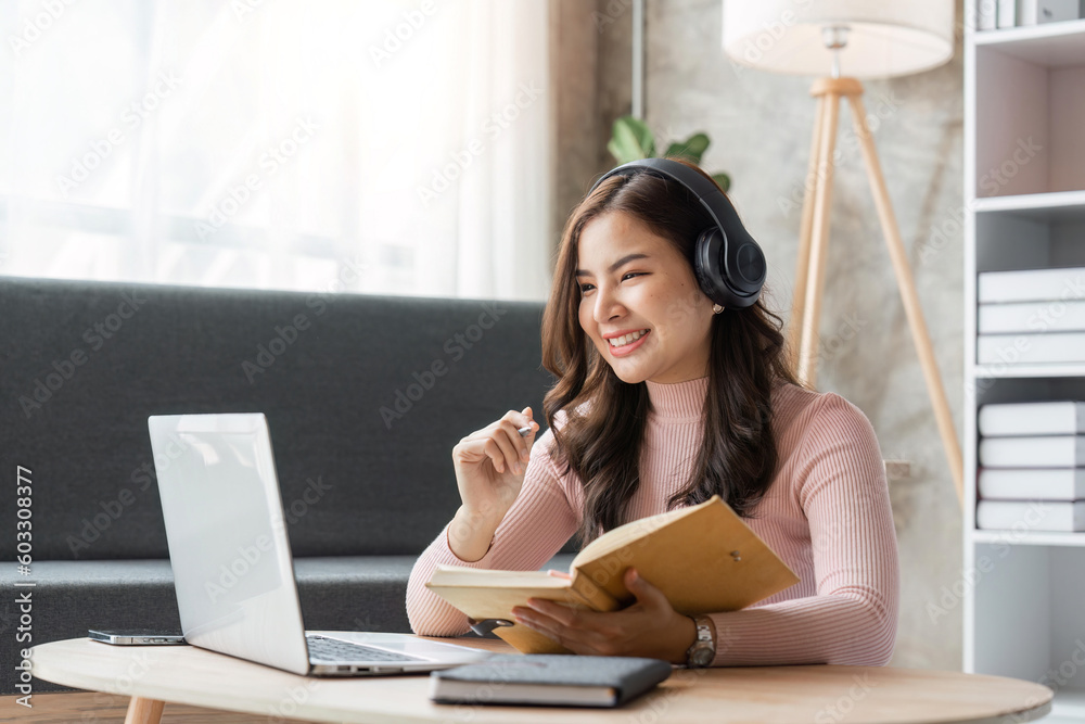 Obraz premium woman taking notes in notebook while using laptop at home in living room. Focused lady writing in notepad