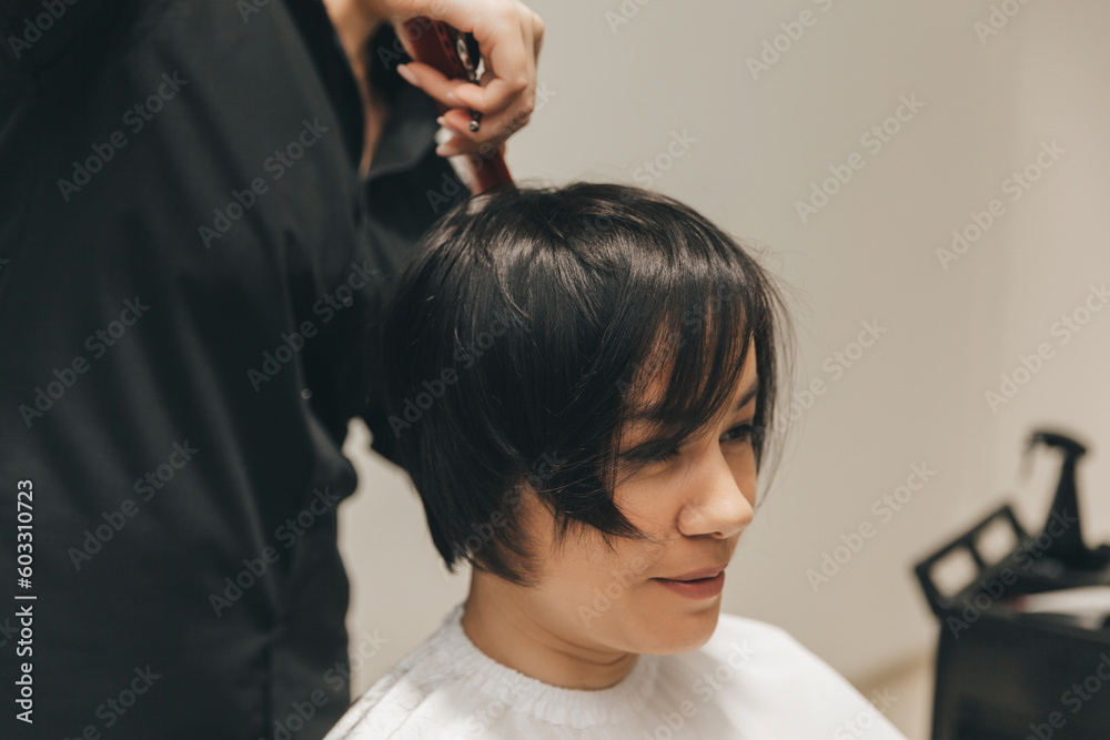 hairdresser makes a haircut to a woman in the salon. The hairdresser cuts wet hair, combing with a comb. client with short hair. back view hairdresser makes a haircut to a woman in the salon. The hairdresser cuts wet hair, combing with a comb. client with short hair. back view