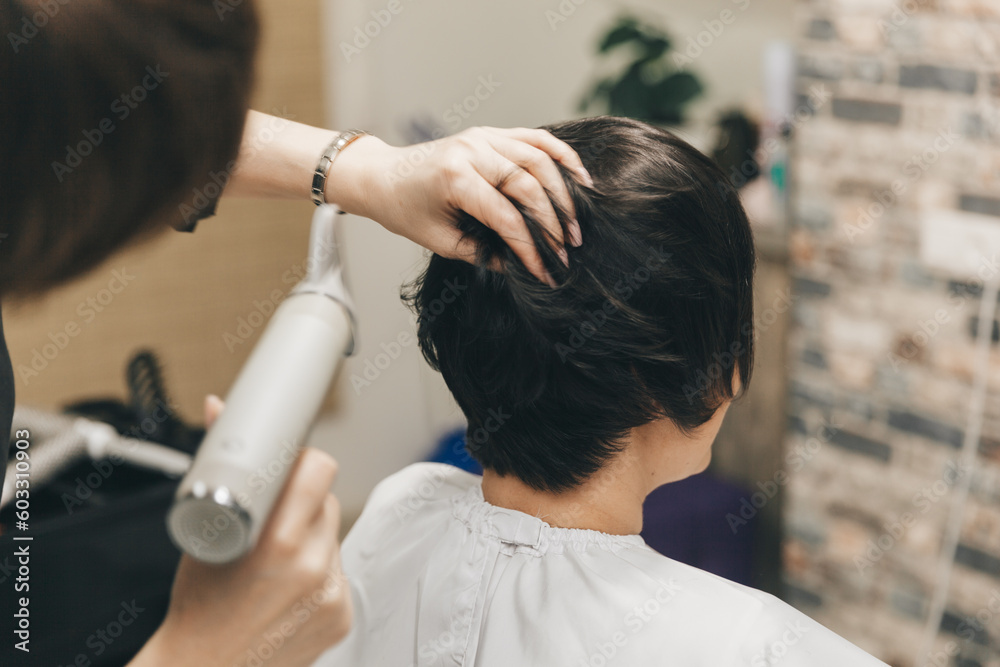 Obraz premium Close-up of the hands of a hairdresser drying women's hair with a hairdryer. short haircut and styling
