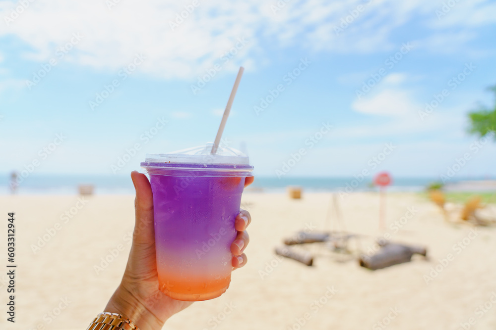 Hand holding summer cold drink orange blueberry fruit soda with blue sky and beach sea background. Calmness and relaxation concept. Hand holding summer cold drink orange blueberry fruit soda with blue sky and beach sea background. Calmness and relaxation concept.