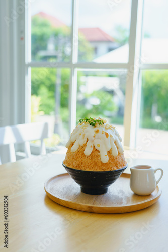 Japanese shaved ice dessert , milk tea kakigori bingsu topped with sweet whipping cream almond stick Thai tea sauce condensed milk on table in cafe. Traditional summer dessert menu in Japan.