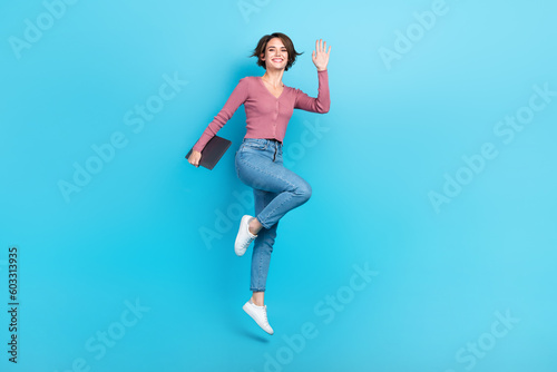 Full size photo of gorgeous cheerful girl hand hold netbook jumping isolated on blue color background © deagreez