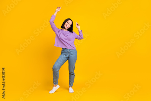 Full length photo of good mood woman wear purple shirt jeans shoes enjoy dancing raising hands isolated on yellow color background © deagreez