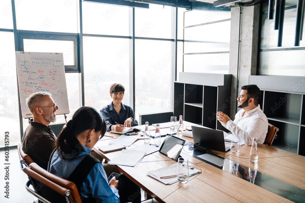 Side view of smiling multiethnic team gathered around table discussing project in office