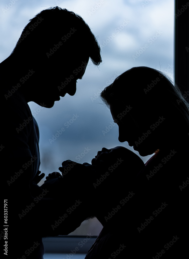 Silhouette of loving couple with newborn. Happy parents holding baby.