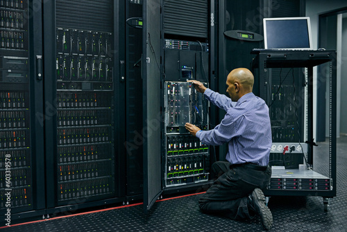 Database, software and a man engineer in a server room for cybersecurity maintenance on storage hardware. Computer network or mainframe with a technician working on information technology equipment photo