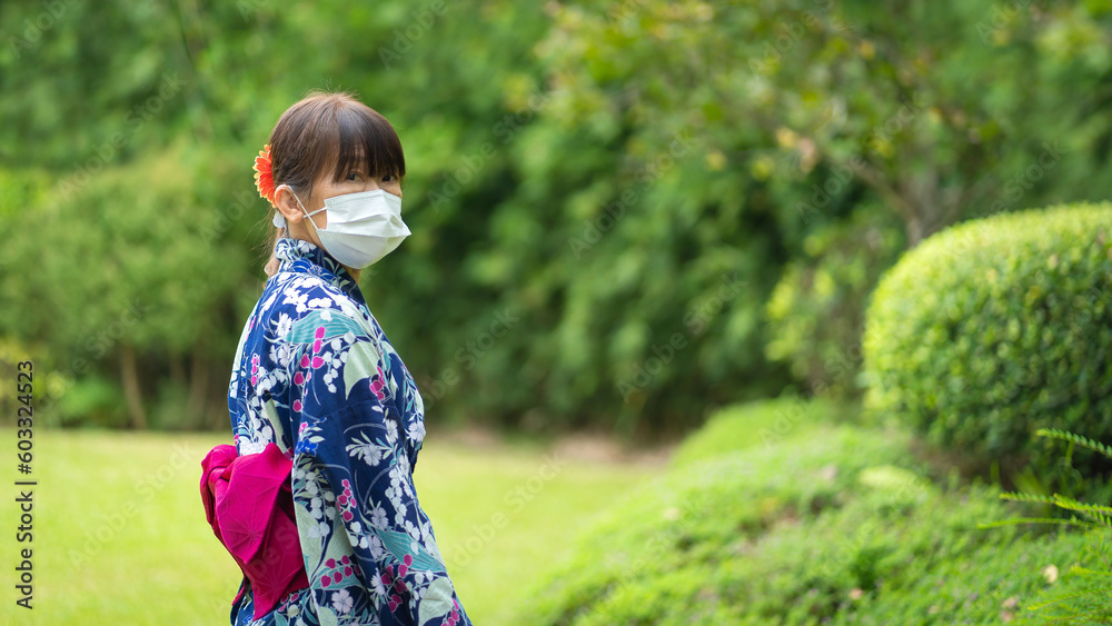 Cute Japanese women wearing beautiful traditional clothes dress walking relax happily in casual Yukata kimonos with white masks and red umbrellas in a fresh green natural garden. Cute Japanese women wearing beautiful traditional clothes dress walking relax happily in casual Yukata kimonos with white masks and red umbrellas in a fresh green natural garden.