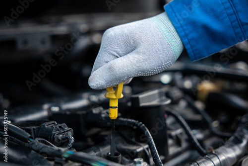 Mechanic checking car oil level with a gauge while standing next to an open hood. Expert examining engine oil for maintenance and safety purposes.