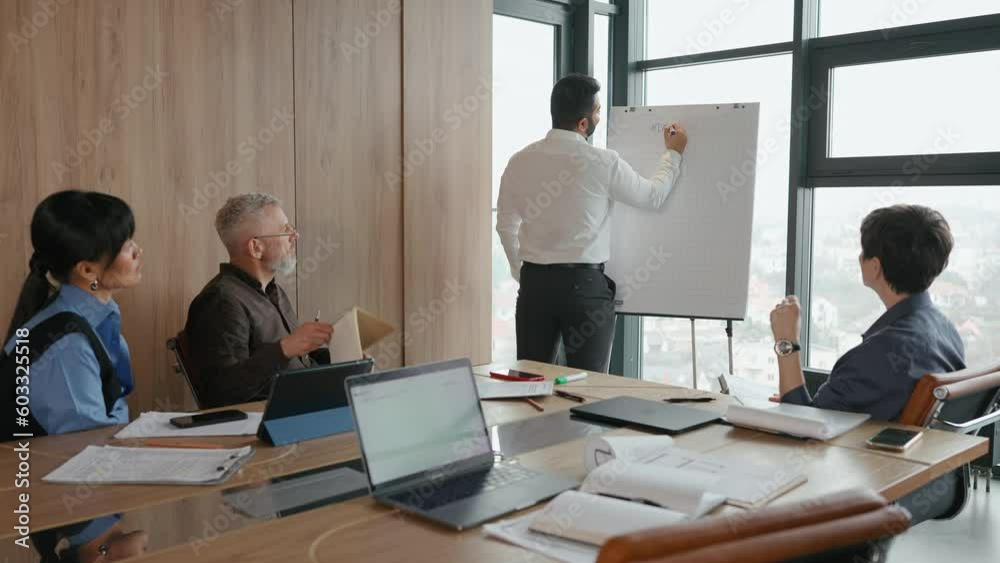 Concentrated multinational colleagues look at indian worker who writes on blackboard in office Concentrated multinational colleagues look at indian worker who writes on blackboard in office