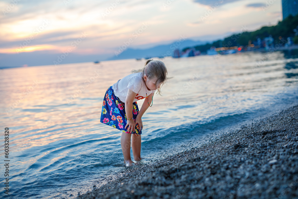 Little girl walking on beautiful ocean beach. Happy preschool child play by sunset on sea beach. Family vacations with children in summer.