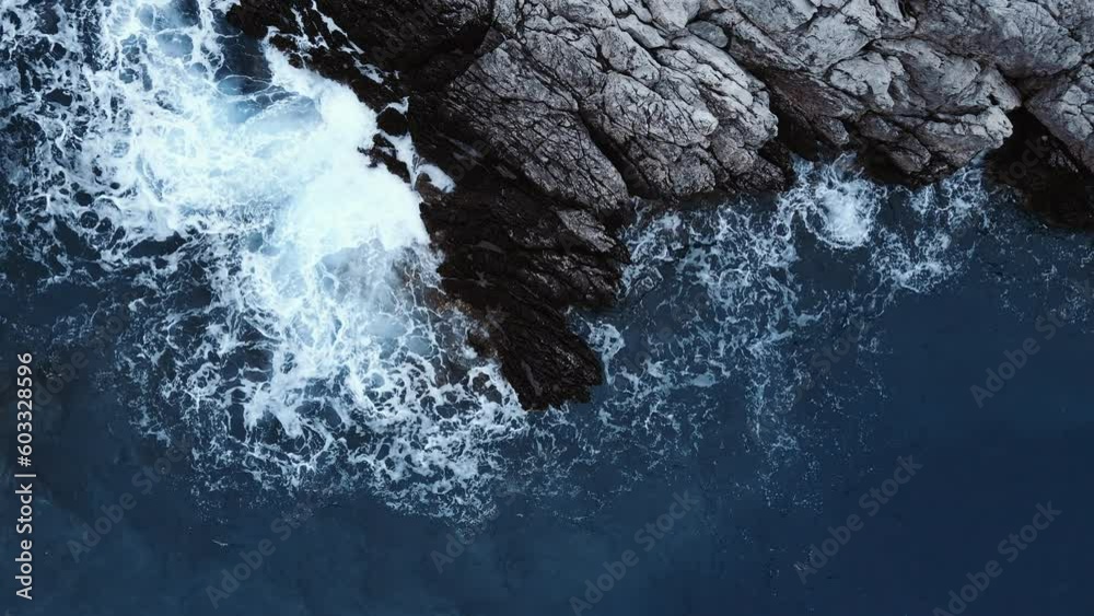 Drone above of turquoise ocean waves crashing and white foaming on huge reef rock stones. Wild sea washing reef rock cliff