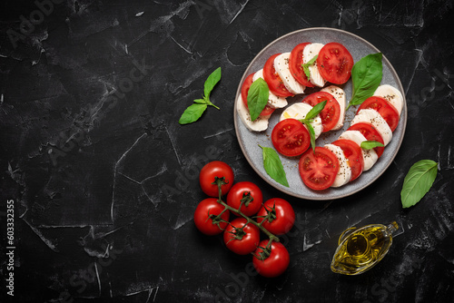 Italian caprese salad with chopped tomatoes, mozzarella, basil, olive oil on a black stone background. Top view, flat lay