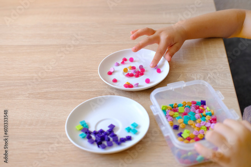 small child, toddler sorts small plastic chips by color, kid's fingers close-up, concept development fine motor skills, tactile sensations, creativity, children's entertainment, color perception