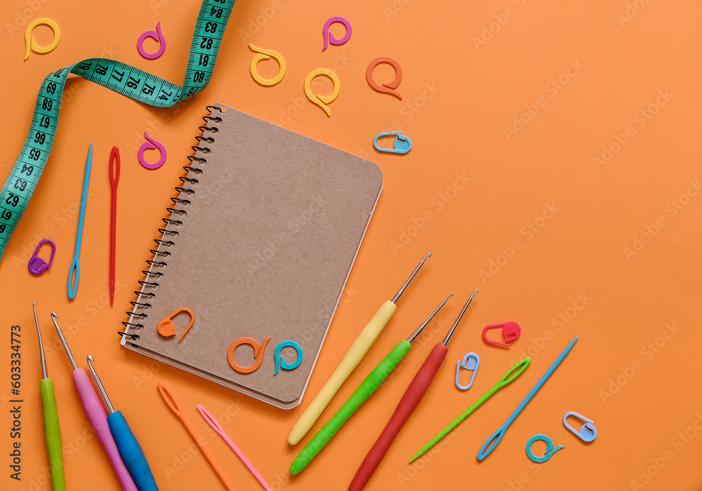 Notebook with knitting and crocheting tools on an orange background. Top view. Copy space. Notebook with knitting and crocheting tools on an orange background. Top view. Copy space.
