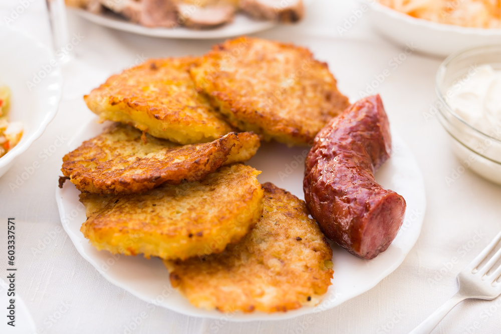 Fried grated potato pancakes with fried sausage on white plate