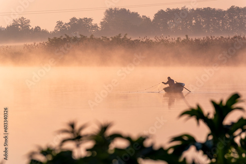 a fisherman casting nets on a boat into the river at dawn.