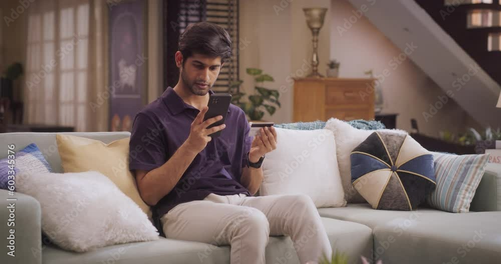 Handsome Indian Man Using Credit Card and Smartphone for Online Shopping at Home. Smiling Happy Guy Purchasing Good at e-Store. e-Commerse Concept. Medium Shot Handsome Indian Man Using Credit Card and Smartphone for Online Shopping at Home. Smiling Happy Guy Purchasing Good at e-Store. e-Commerse Concept. Medium Shot